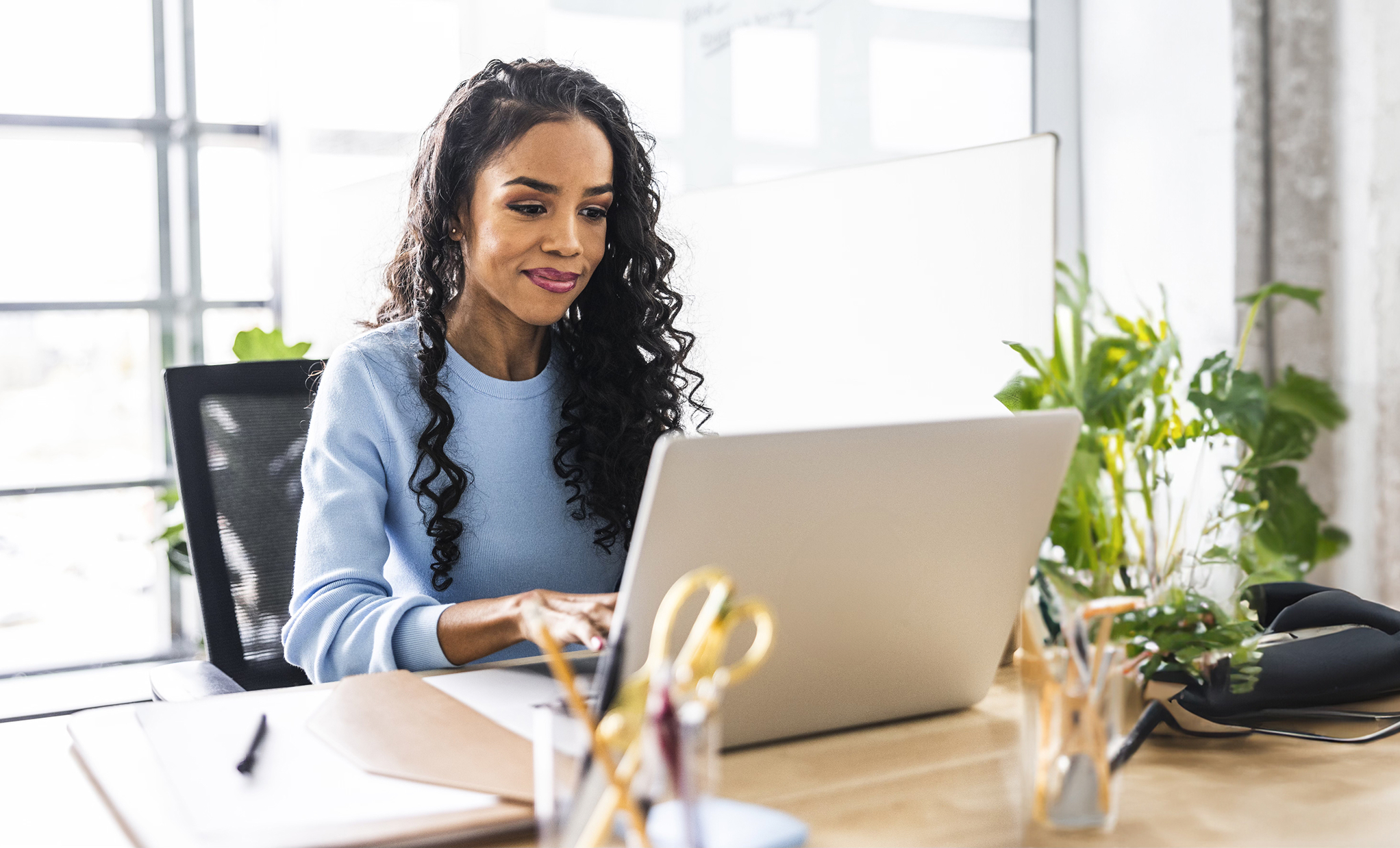 Person sitting at a desk and working on a laptop in a bright office.